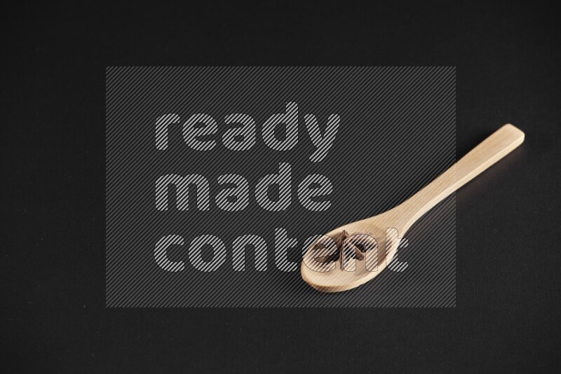 Star Anise in a wooden spoon on more stars anise filling the frame on black flooring