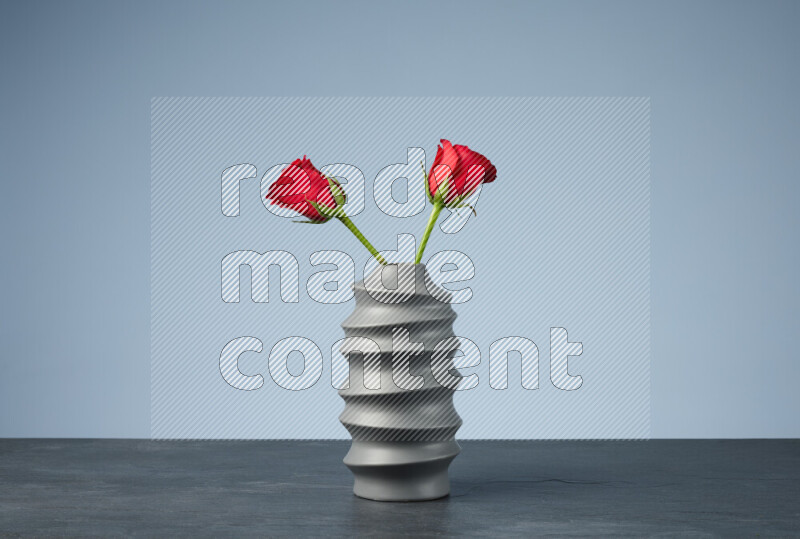 An arrangement of vivid red roses in a grey spiral vase on black marble background