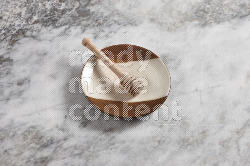 Multicolored pottery plate with wooden honey dipper in it on grey marble background