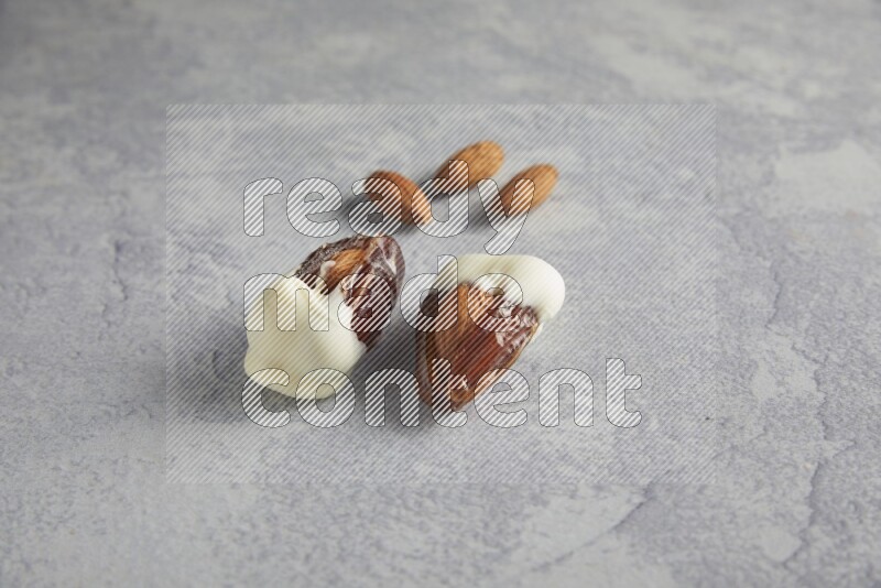 two almonds stuffed dates covered with white chololate with unroasted almonds on a light grey background