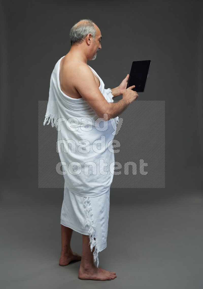 A man wearing Ehram Standing working on tablet on gray background