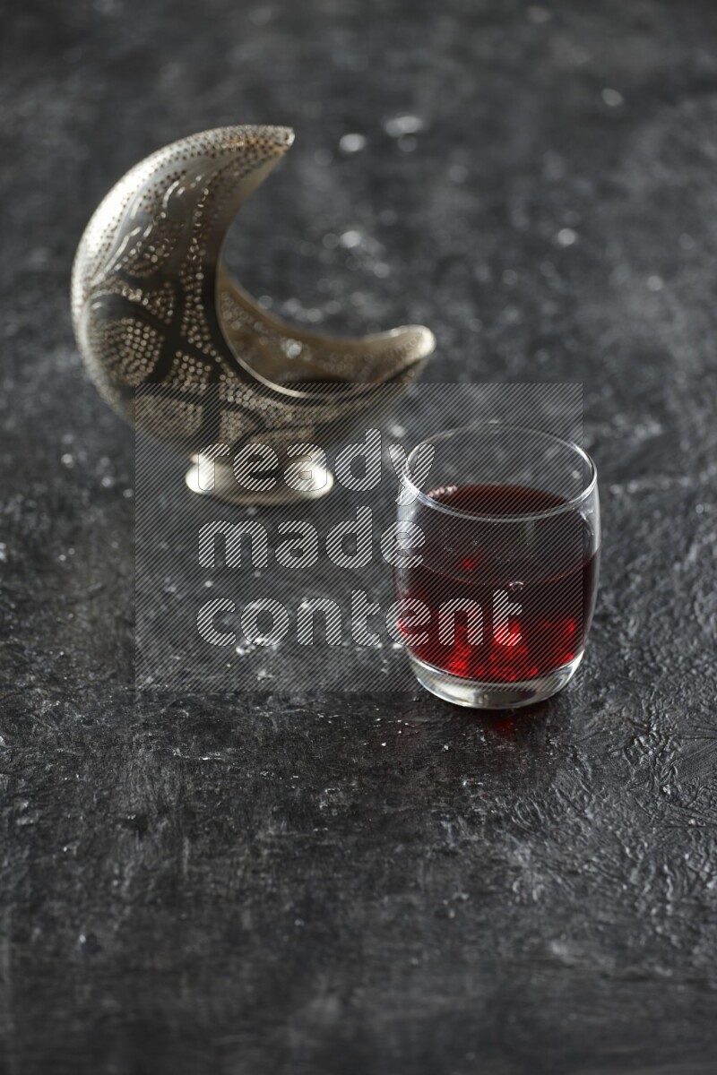 A silver lantern with different drinks, dates, nuts, prayer beads and quran on textured black background