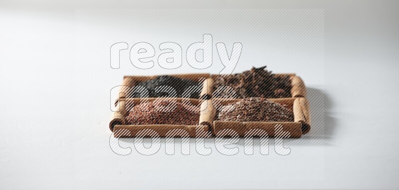 4 squares of cinnamon sticks full of black seeds, cloves, flaxseeds and garden cress on white flooring