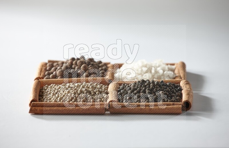 4 مربعات من أعواد القرفة ممتلئة ببهار الفلفل الحلو والملح الأبيض والفلفل الأبيض والفلفل الأسود على أرضية بيضاء