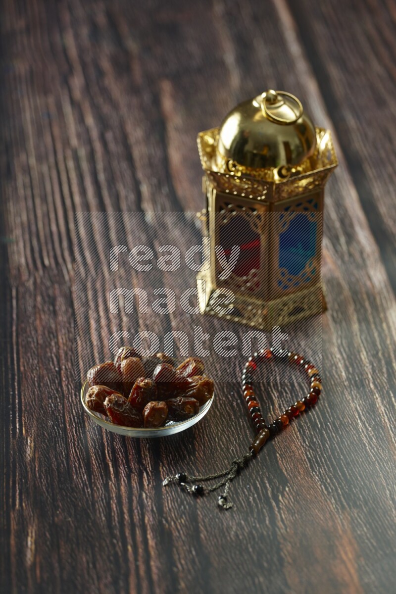 A golden lantern with different drinks, dates, nuts, prayer beads and quran on brown wooden background