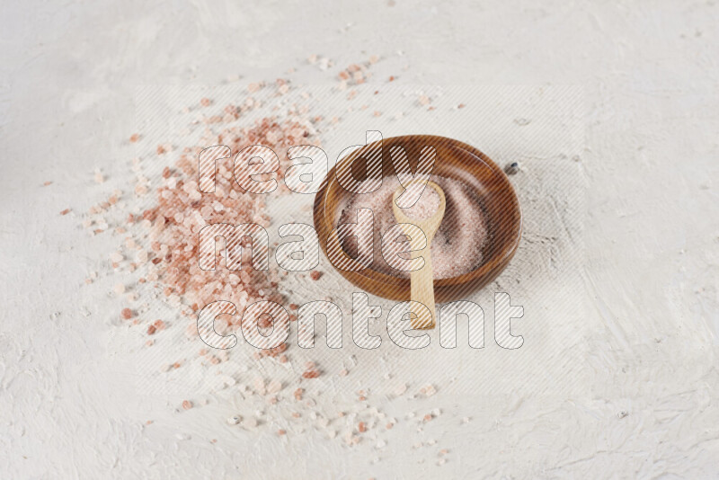 A pottery plate full of fine salt with bunch of coarse salt beside it on white background