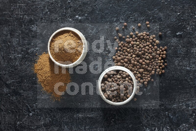 2 beige bowls, one full of allspice powder and the other full of whole balls and both spread on a textured black flooring
