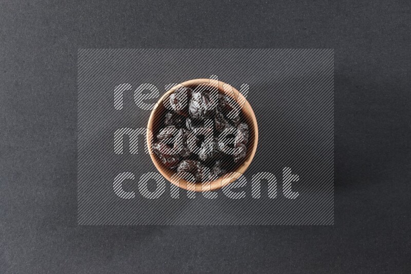 A wooden bowl full of dried plums on a black background in different angles