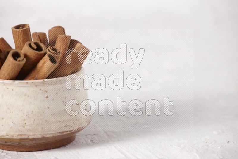 Cinnamon sticks in a beige bowl on a white background