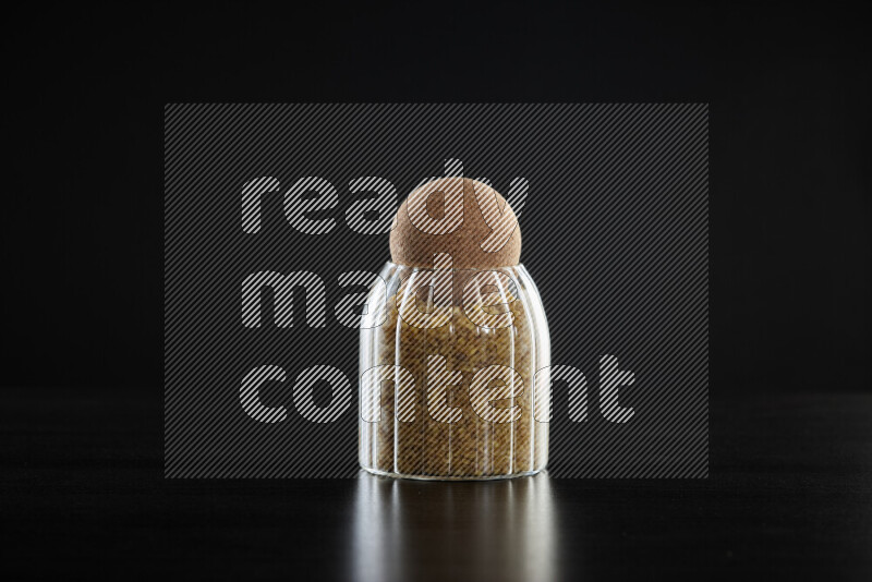 Coarse bulgur in a glass jar on black background