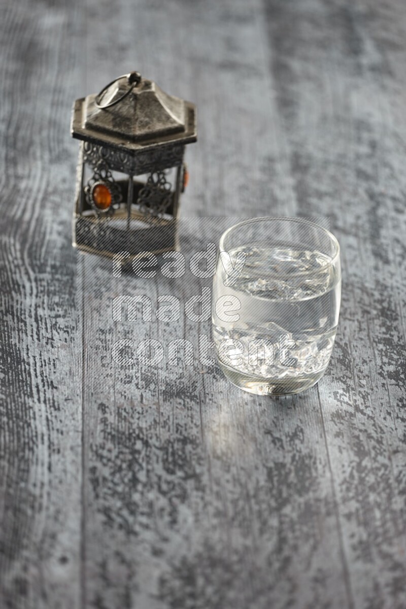 A silver lantern with different drinks, dates, nuts, prayer beads and quran on grey wooden background