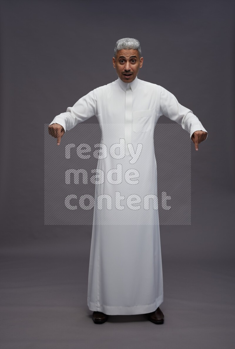 Saudi man wearing thob standing interacting with the camera on gray background