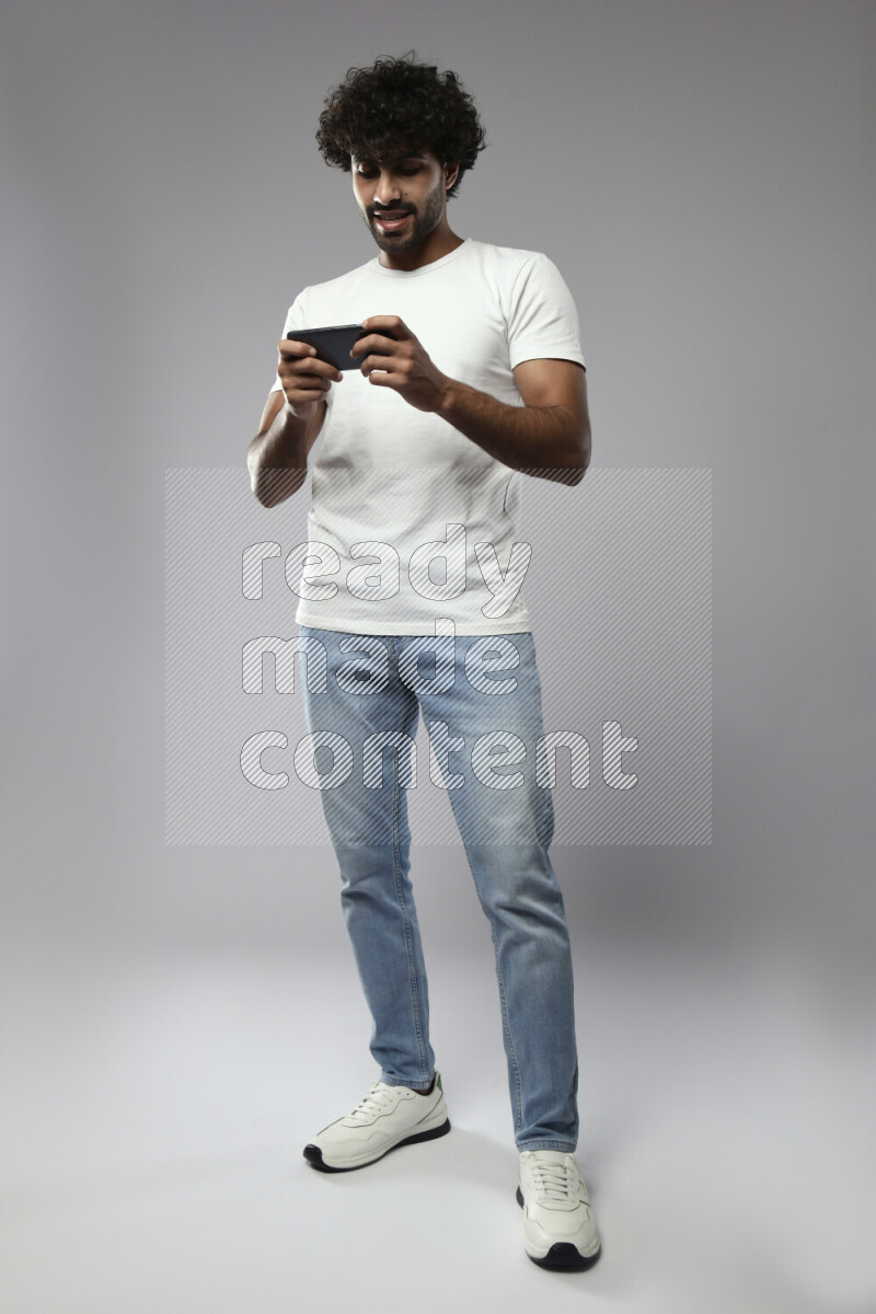 A man wearing casual standing and gaming on the phone on white background