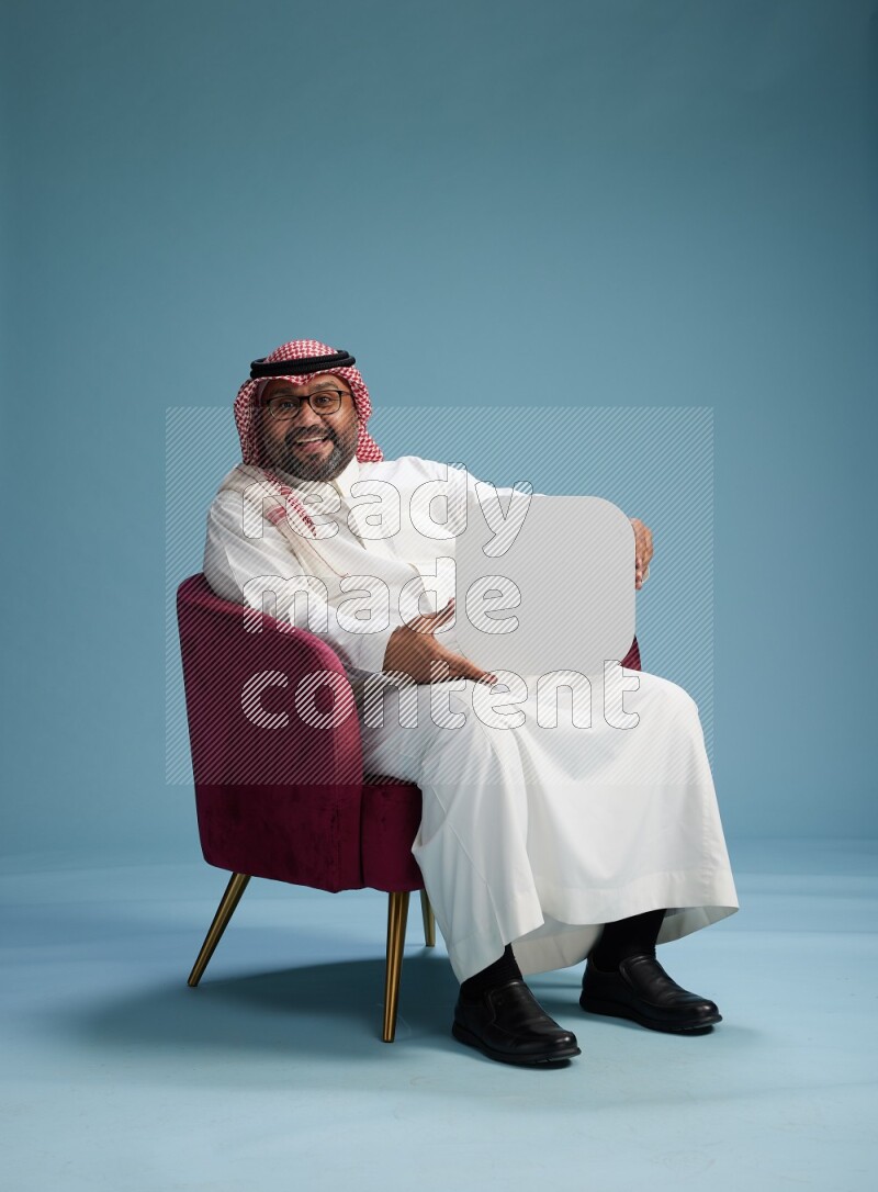 Saudi Man with shimag sitting on chair holding social media sign on blue background