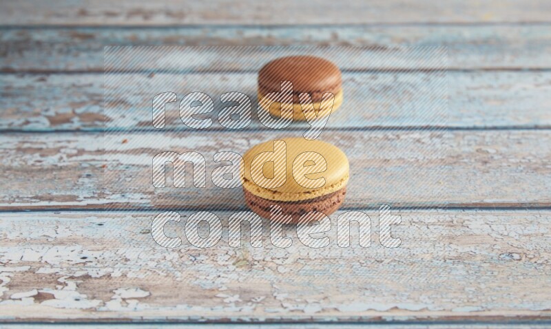 45º Shot of two Yellow and Brown Chai Latte macarons on light blue wooden background