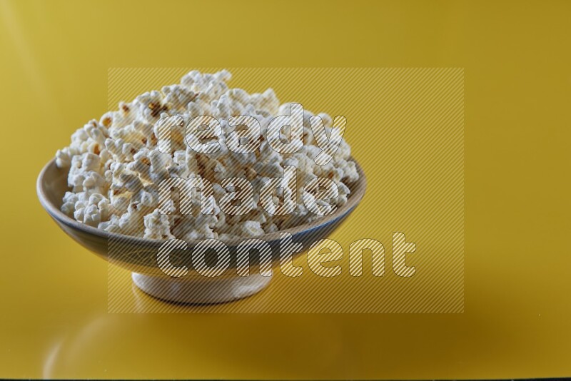 A multicolored ceramic plate full of popcorn on a yellow background in different angles
