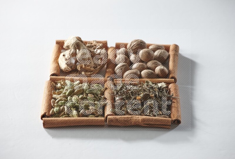4 مربعات من أعواد القرفة ممتلئة بجوزة الطيب والزنجبيل المجفف والهيل والريحان المجفف على أرضية بيضاء