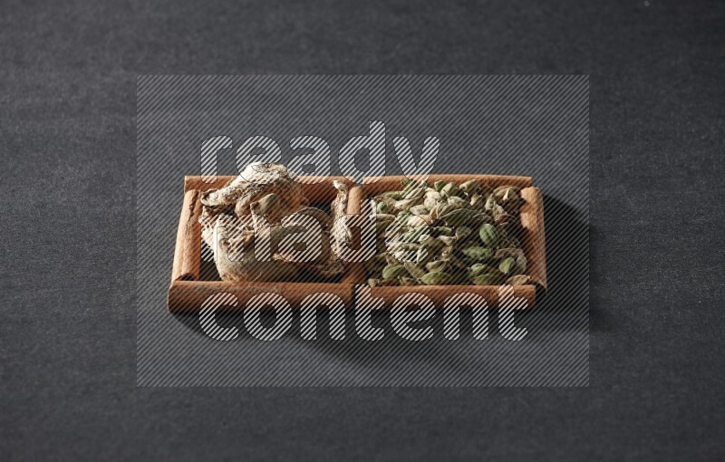 مربعان من أعواد القرفة ممتلئان بحبوب الهيل والزنجبيل المجفف علي خلفية سوداء