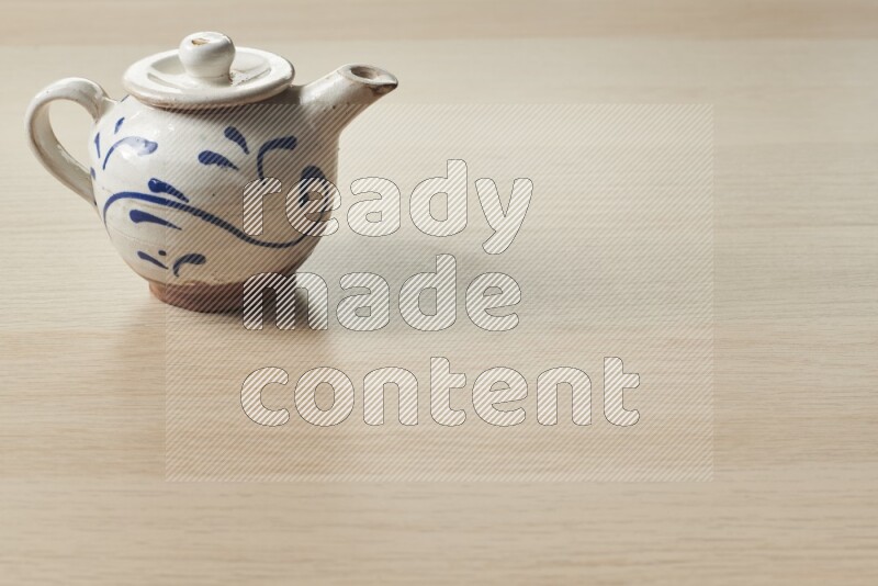 A pottery teapot on light wooden background