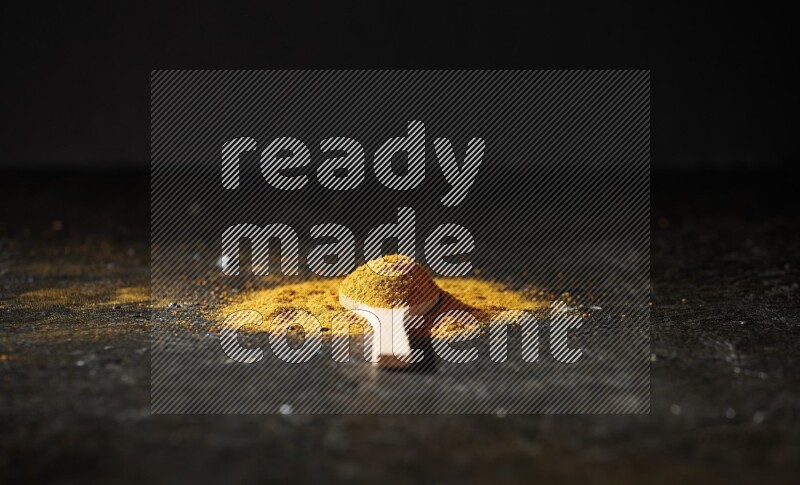 A wooden spoon full of turmeric powder on textured black background