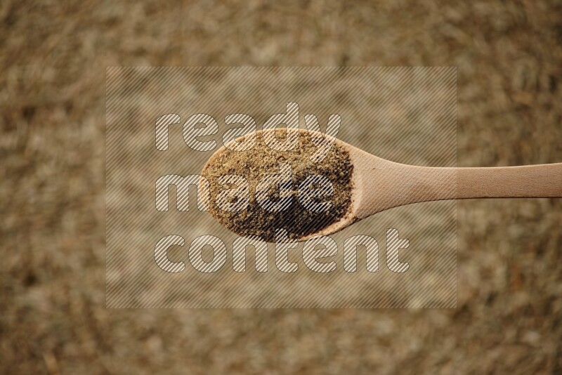 A wooden spoon full of cumin powder on a cumin seeds background