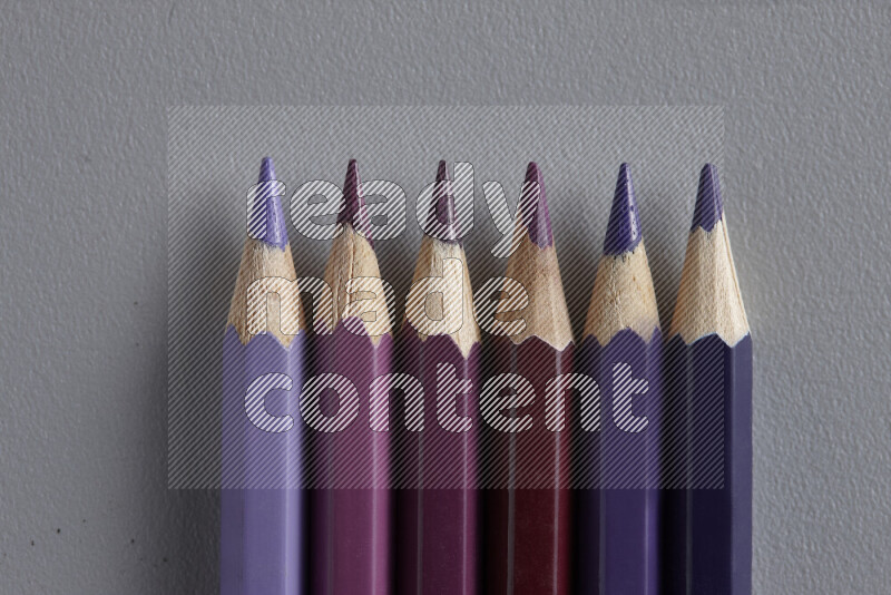 A collection of colored pencils arranged showcasing a gradient of purple hues on grey background