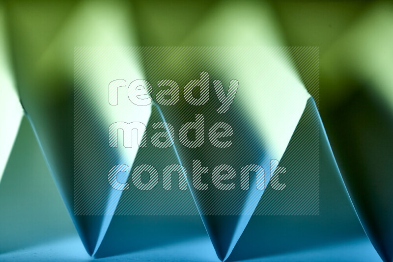 A close-up abstract image showing sharp geometric paper folds in green and blue gradients