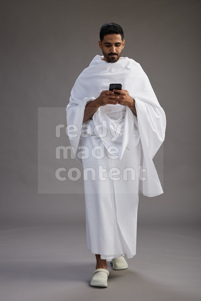 A man wearing Ehram Standing texting on phone on gray background