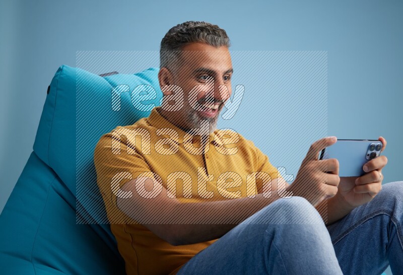 A man sitting on a blue beanbag and playing on phone