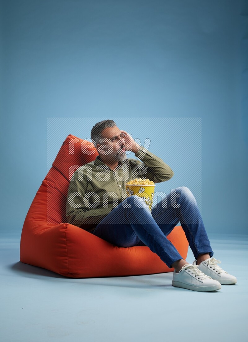 A man sitting on an orange beanbag and eating popcorn