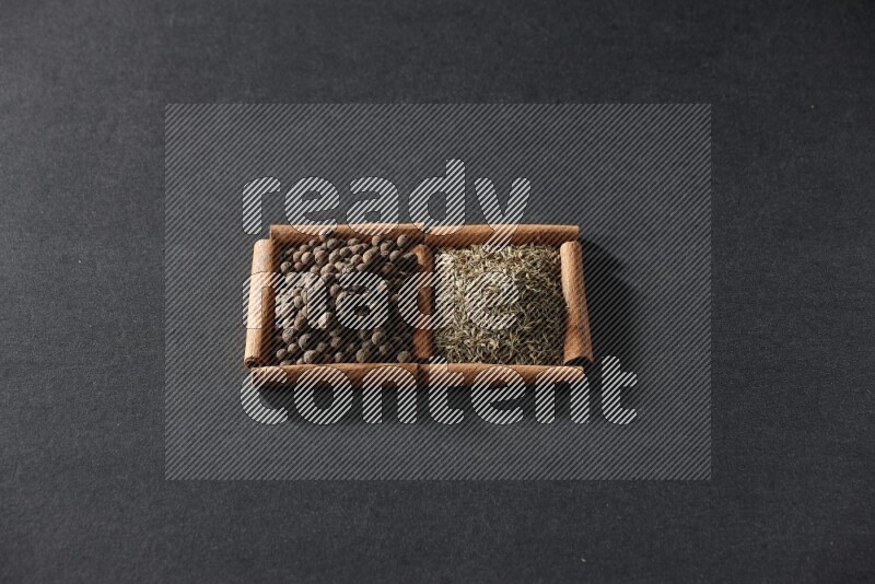 مربعان من أعواد القرفة ممتلئان بحبوب الكمون وحبوب بهار الفلفل الحلو علي خلفية سوداء