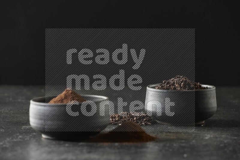 وعاءين من الفخار الأسود أحدهما ممتلئي بحبوب القرنفل والآخر ممتلئ ببودرة القرنفل على خلفية سوداء