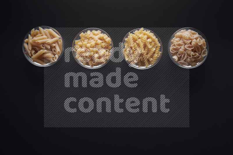 Different pasta types in glass bowls on black background