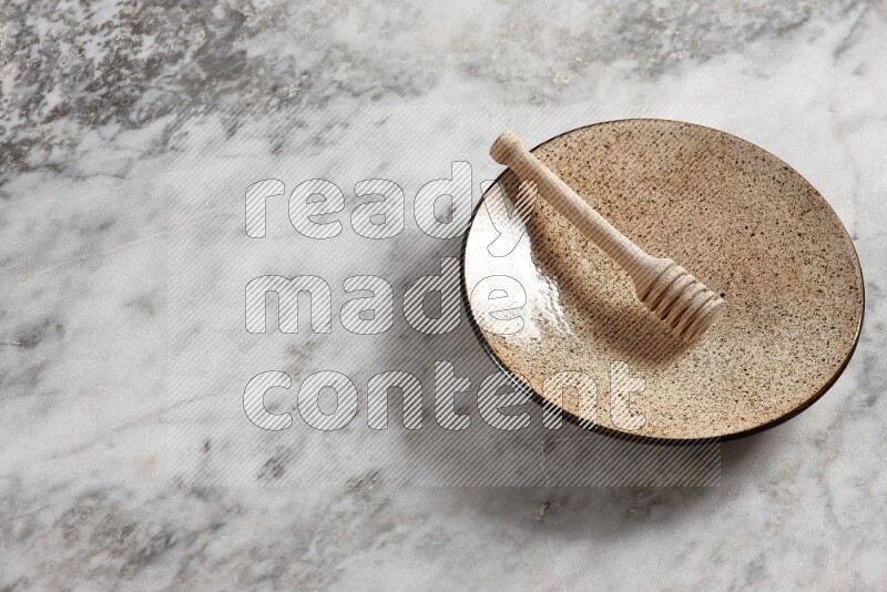 Multicolored pottery plate with wooden honey dipper in it on grey marble background