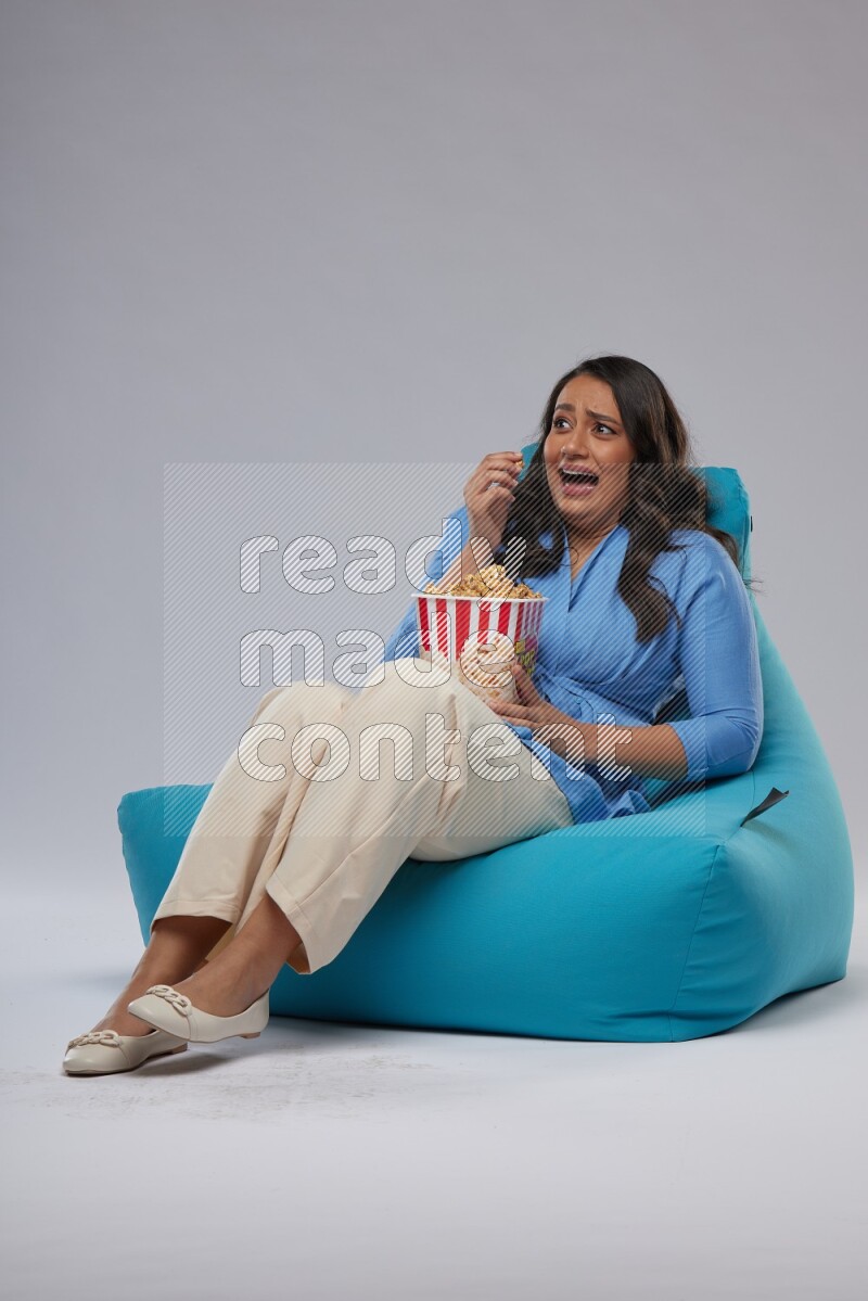 A woman sitting on a blue beanbag and eating popcorn