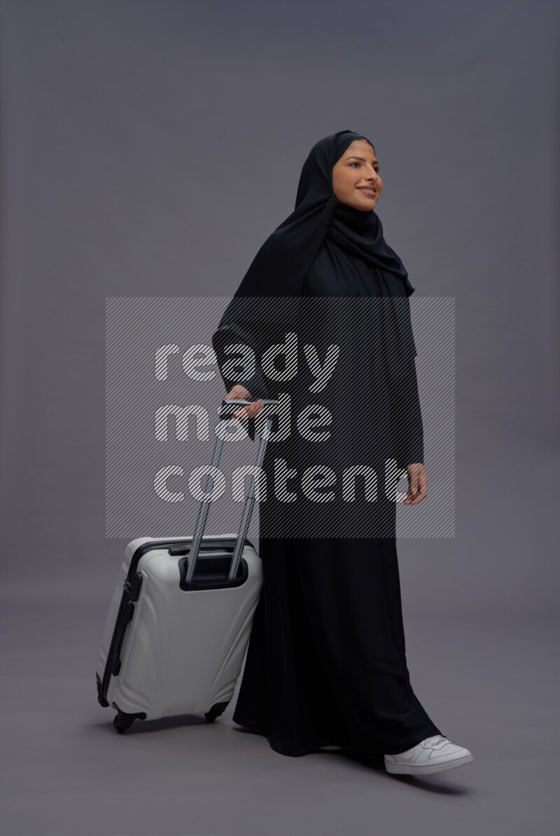 Saudi woman wearing Abaya standing holding bag on gray background