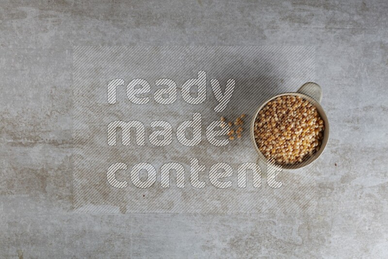corn kernel in a off-white handheld ceramic bowl on a grey textured countertop