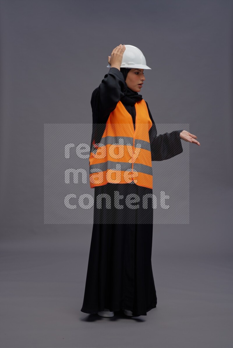 Saudi woman wearing Abaya with engineer vest standing interacting with the camera on gray background