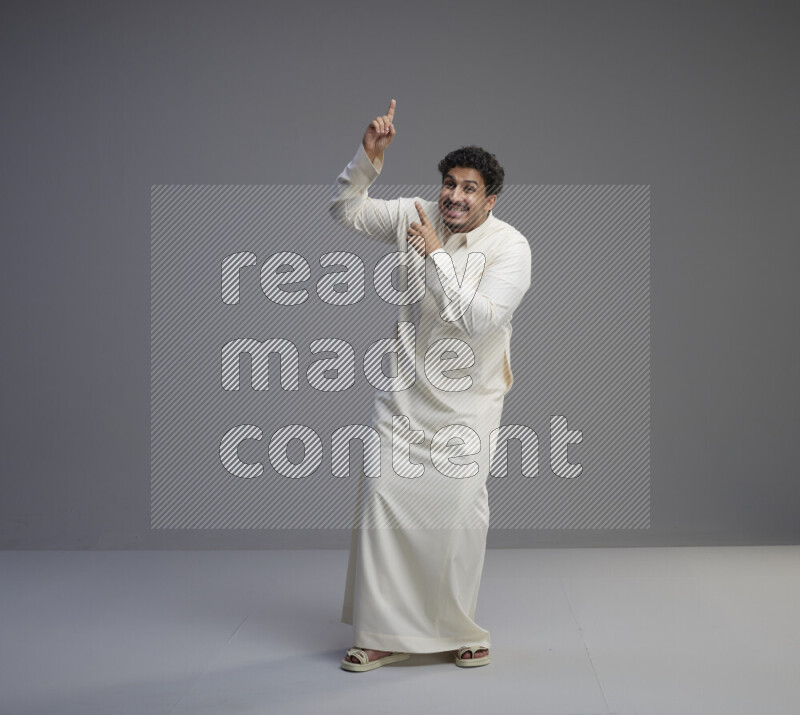 A Saudi man standing wearing thob interacting with the camera on gray background