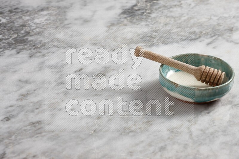 Multicolored pottery bowl with wooden honey dipper in it on grey marble background