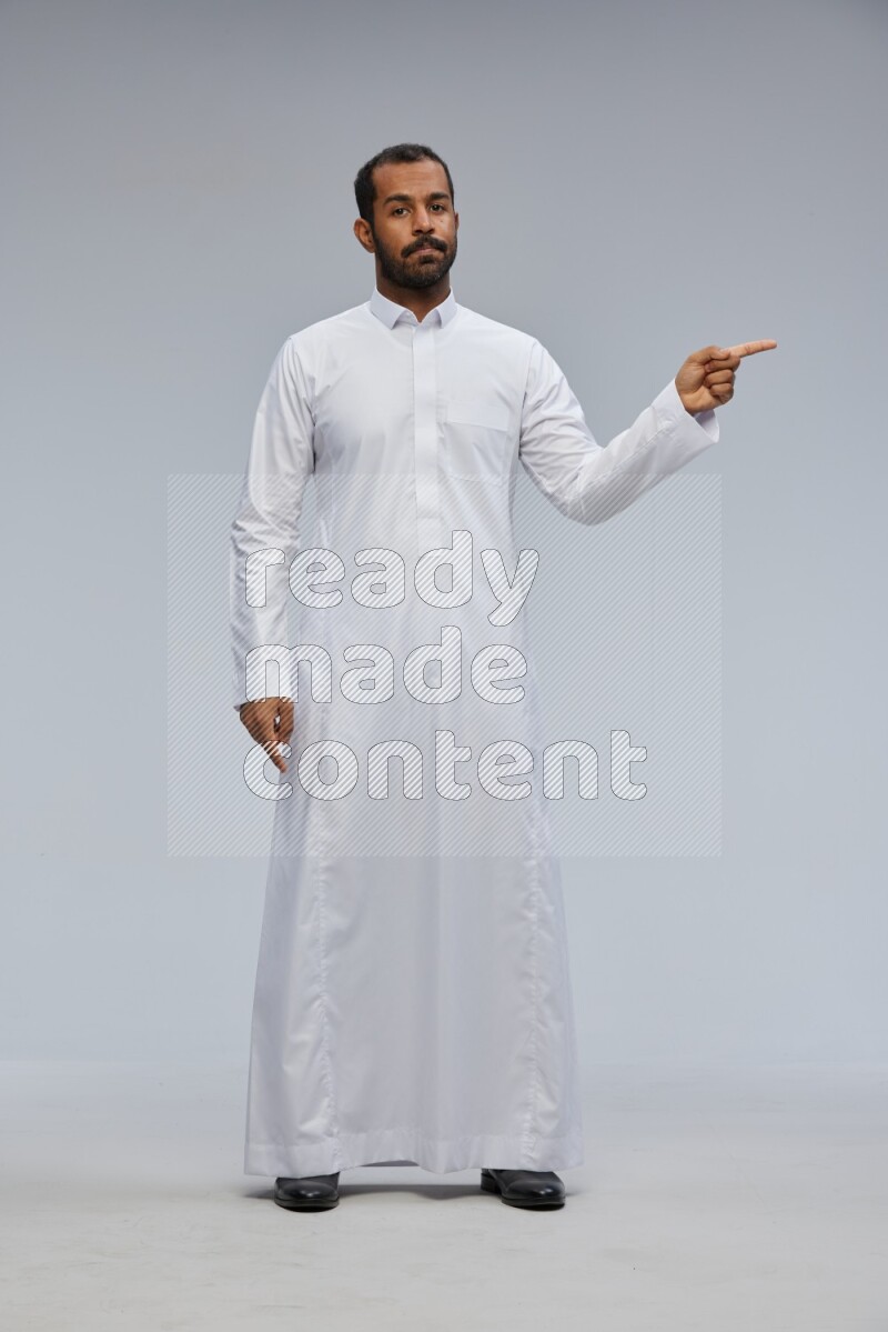 Saudi man Wearing Thob standing interacting with the camera on Gray background