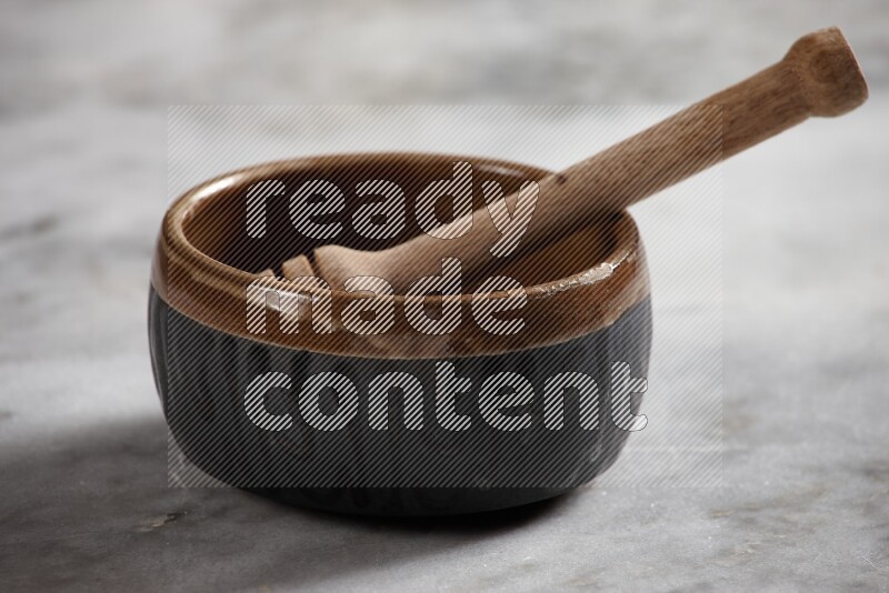 Multicolored pottery bowl with wooden honey dipper in it on grey marble background