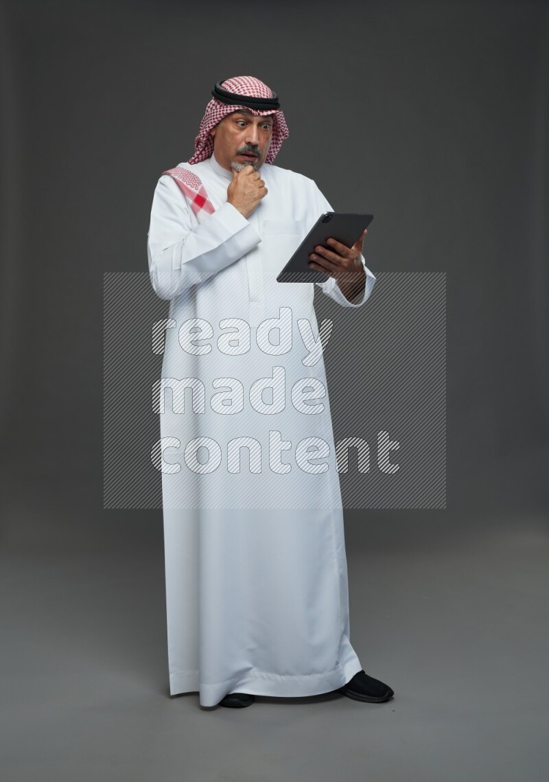 Saudi man with shomag Standing working on tablet on gray background