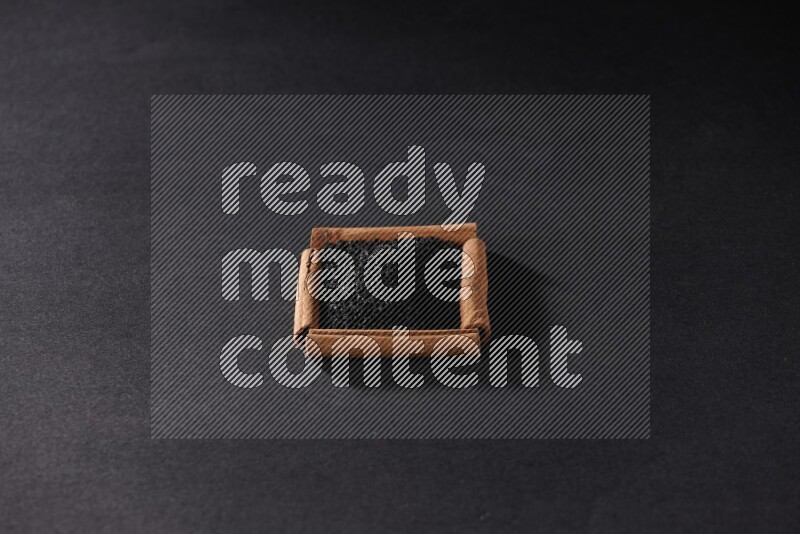 A single square of cinnamon sticks full of black seeds on black flooring