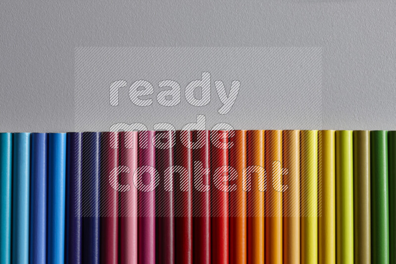 A collection of colored pencils arranged showcasing a gradient of different hues on grey background