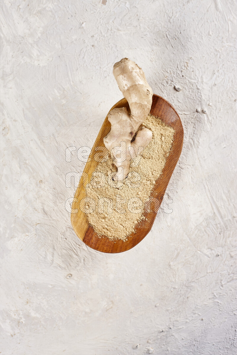 A wooden plate full of ground ginger powder with fresh root in it on white background