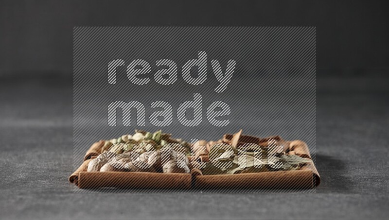 4 squares of cinnamon sticks full of cinnamon, cardamom, bay laurel leaves and nutmegs on black flooring