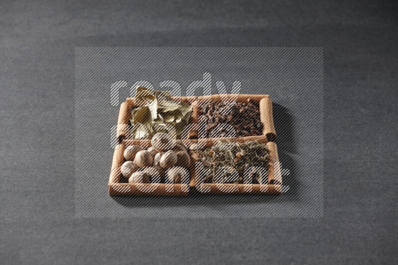 4 مربعات من عيدان القرفة ممتلئة بأوراق الغار والريحان المجفف والقرنفل وجوزة الطيب على أرضية سوداء