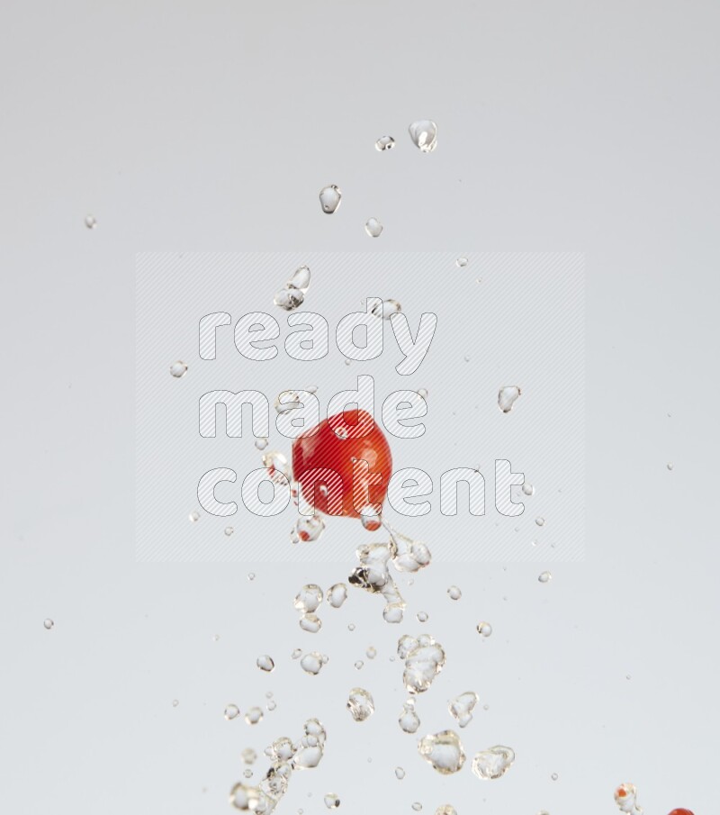 A single cherry tomato flying leaving a splash of water behind on a light blue background