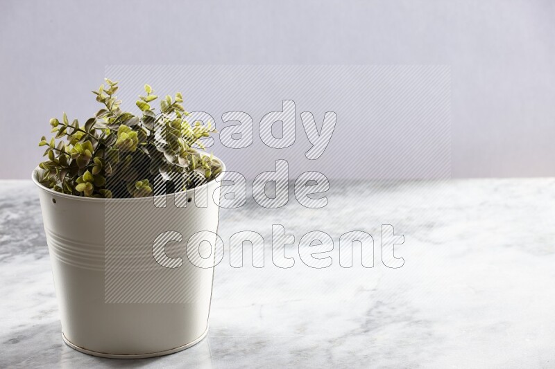 Green artificial plant in white pot on light grey marble background